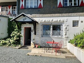 En lille bygning med hvide vægge, en rød dør og et vindue med en metalgitter.