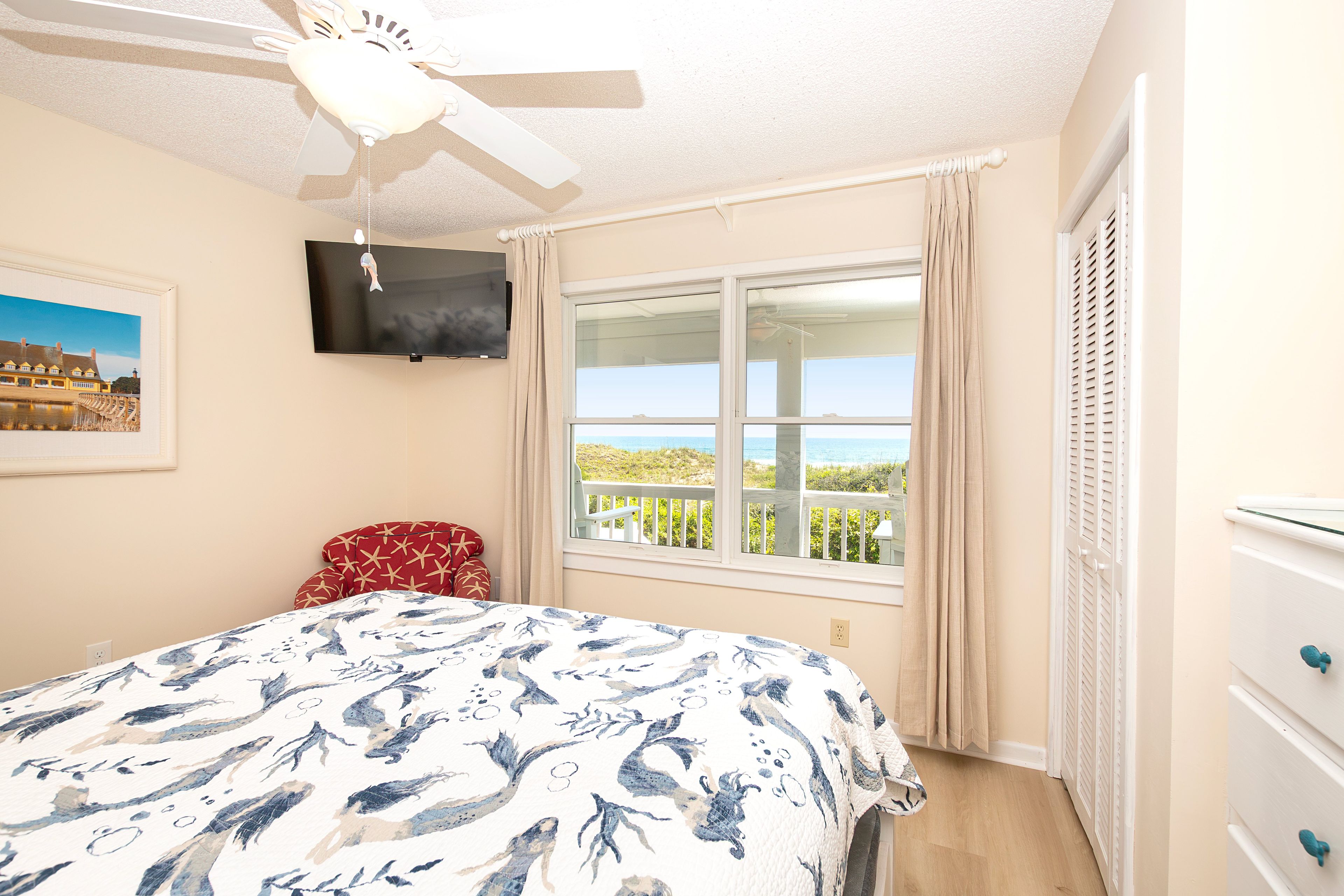 A bedroom with a bed, a ceiling fan, a TV, a window with a view, and a dresser.
