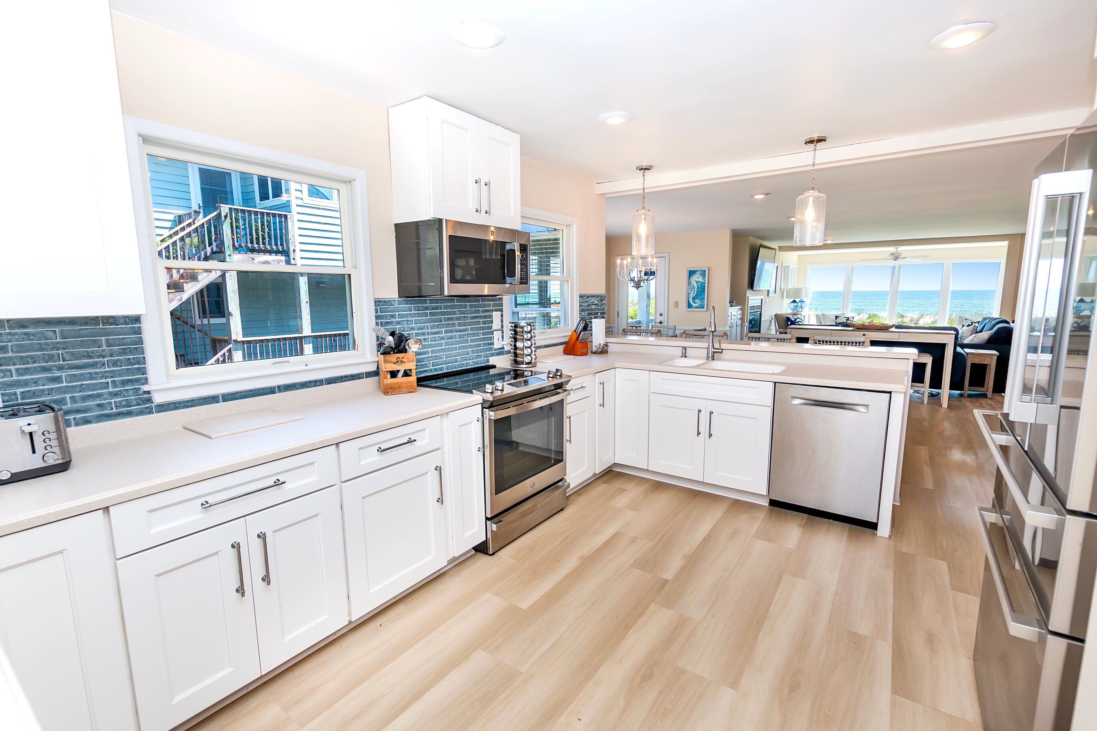 A modern kitchen with white cabinetry, stainless steel appliances, and a view of the ocean.