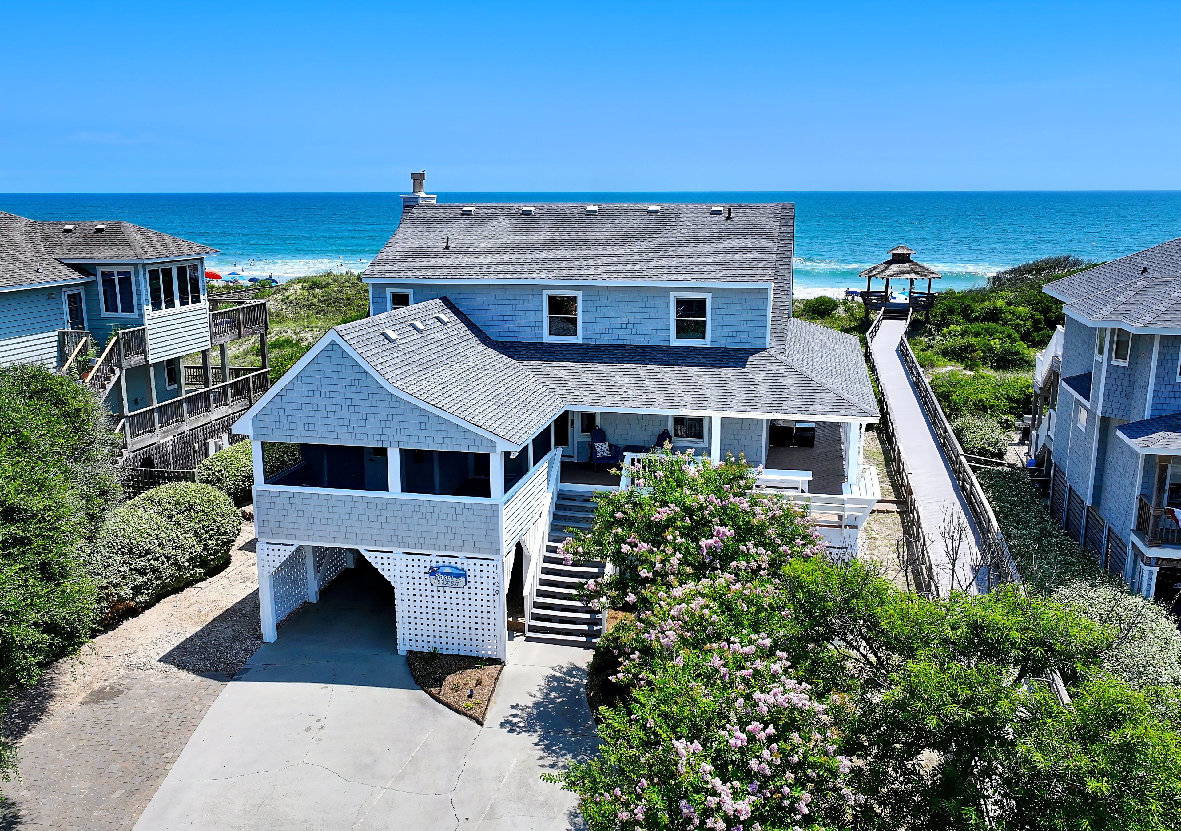 A beachfront property with a large house, a covered porch, and a beach access walkway.