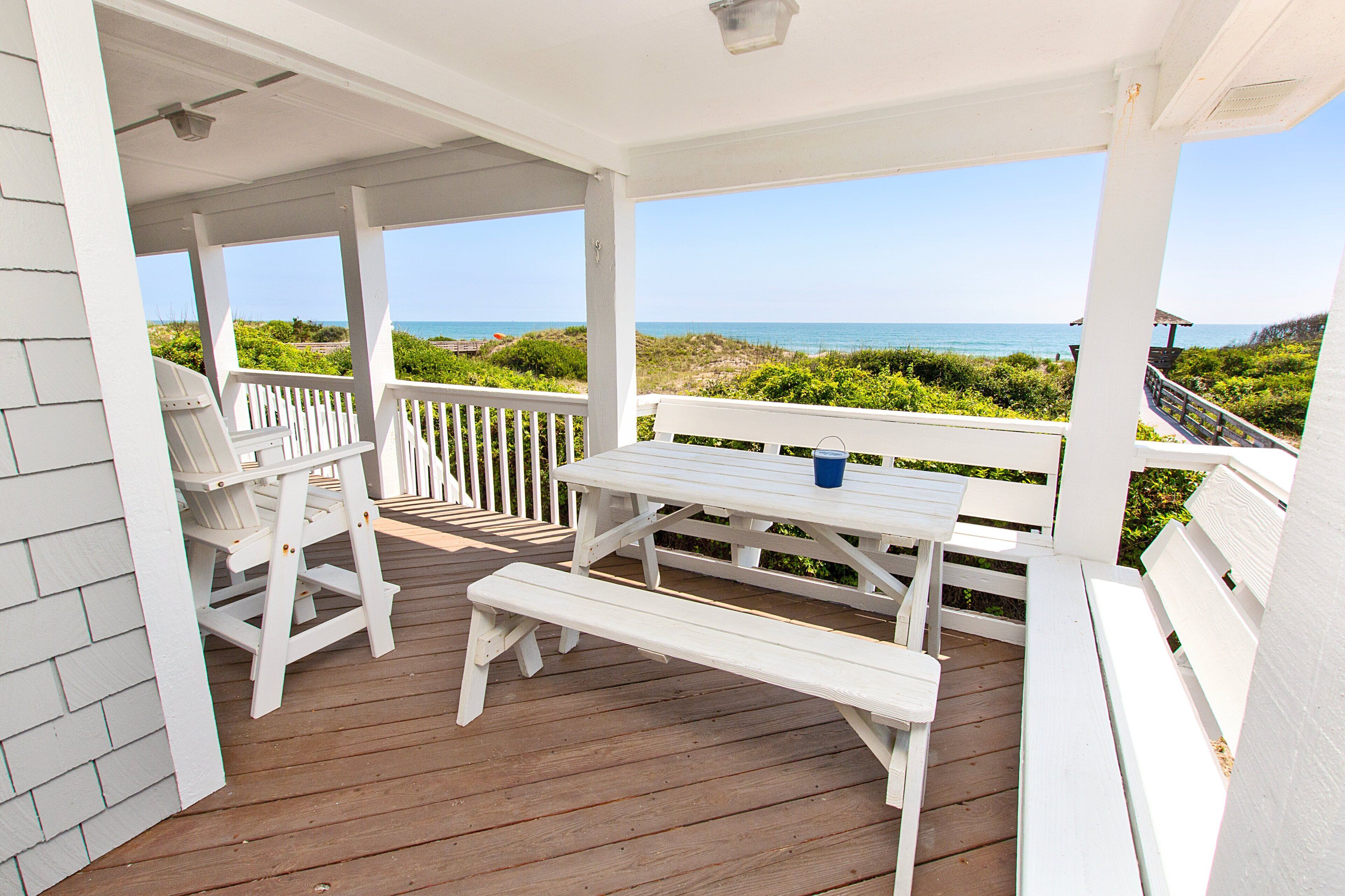 Ein überdachter Außenbereich mit Holzterrasse, weißen Geländern und Blick auf das Meer.
