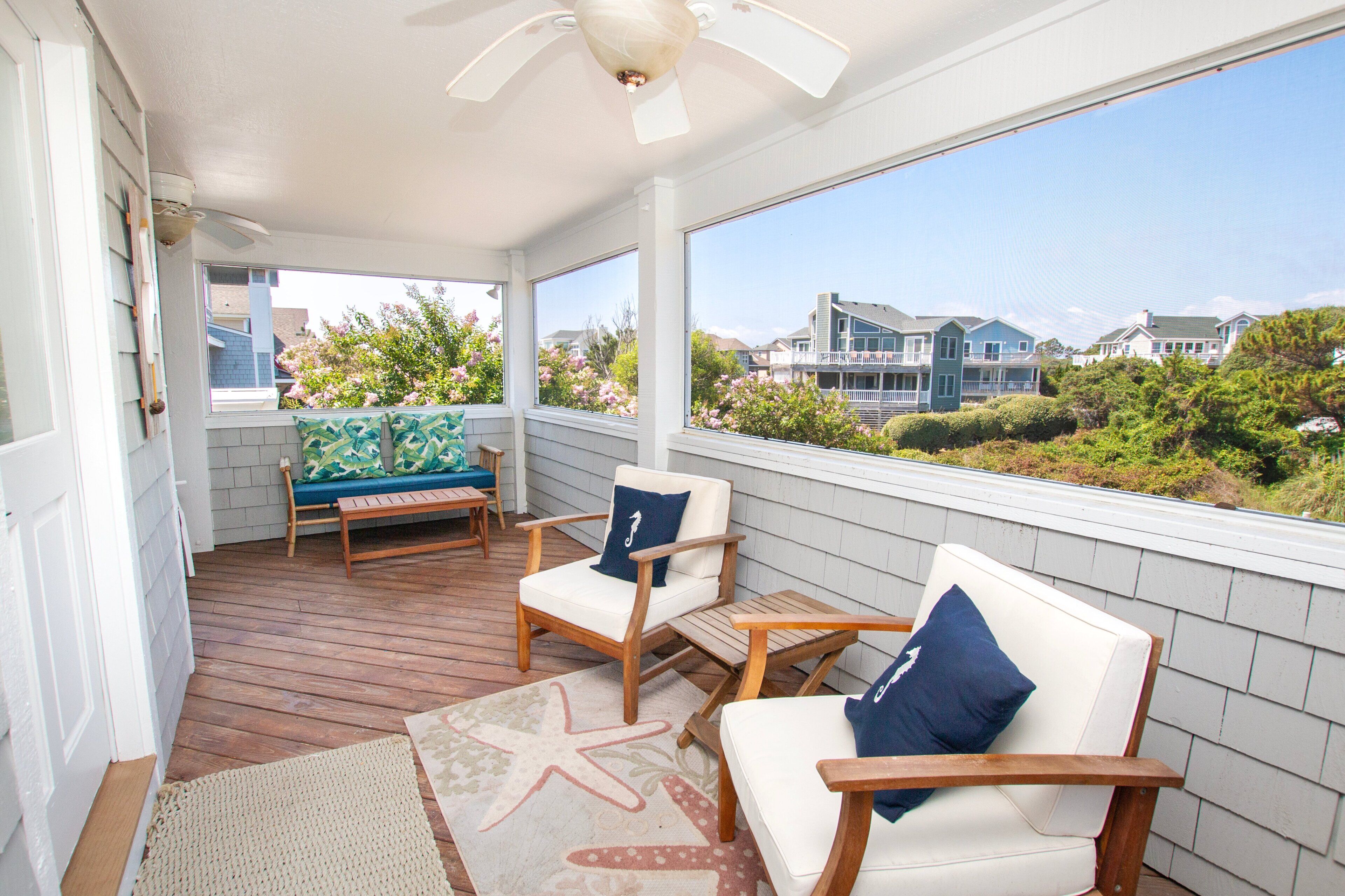 A covered porch with wooden furniture, a starfish rug, and a view of houses in the distance.