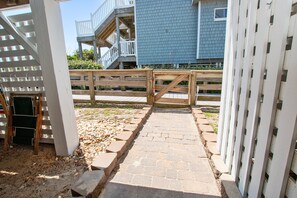 A gated entrance with a wooden gate, a stone pathway, and a building with a blue exterior in the background. - OCEANFRONT, Ocean Views, Hot Tub, Comm Pool -104, Shore Crew (Corolla)