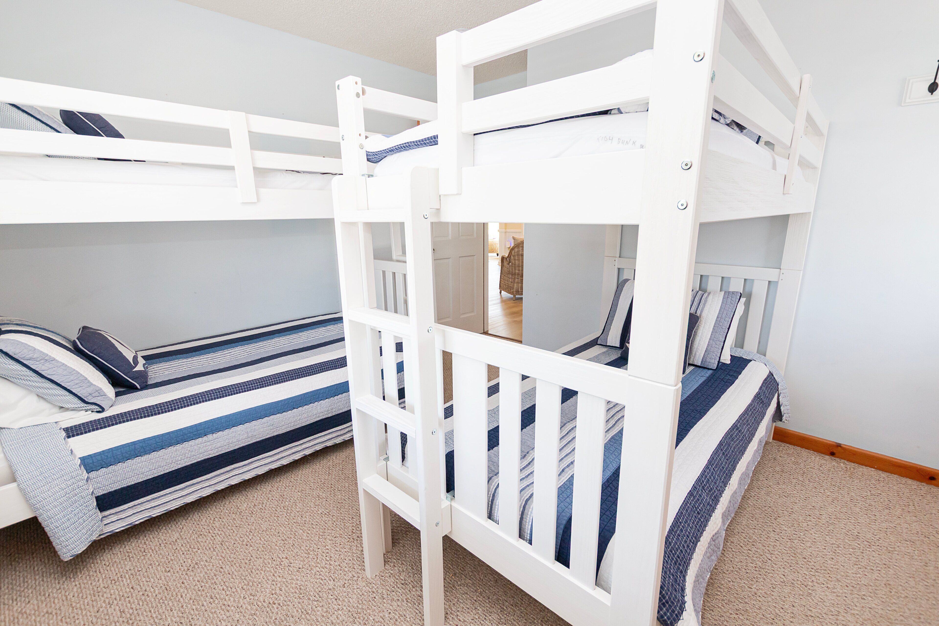 A bunk bed room with a striped bedspread and a visible door leading to another room.