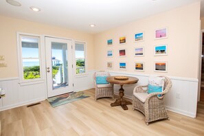 A room with a wooden floor, white walls, a dining table with chairs, and a door leading to a balcony. - OCEANFRONT, Ocean Views, Hot Tub, Comm Pool -104, Shore Crew (Corolla)