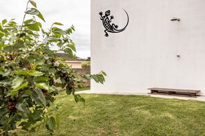 A white wall with a black lizard decal, a grassy lawn, and a wooden bench.