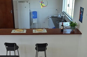 A bar area with two chairs, a water dispenser, a refrigerator, and a window with a view.