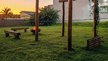 A wooden pergola structure in a grassy outdoor area with a bench and a fire pit.