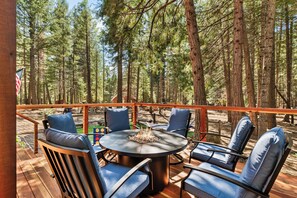 An outdoor deck with a round table and four chairs, surrounded by tall trees.