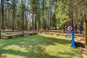 A forested area with a target for archery practice, picnic tables, and a wooden structure.