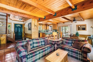 A cozy cabin interior with a plaid sofa set, wooden beams, and a kitchen area.