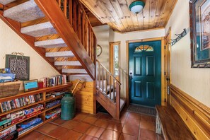 A wooden staircase leading to a door with a stained glass window, a bookshelf filled with books and games, and a green trash can.