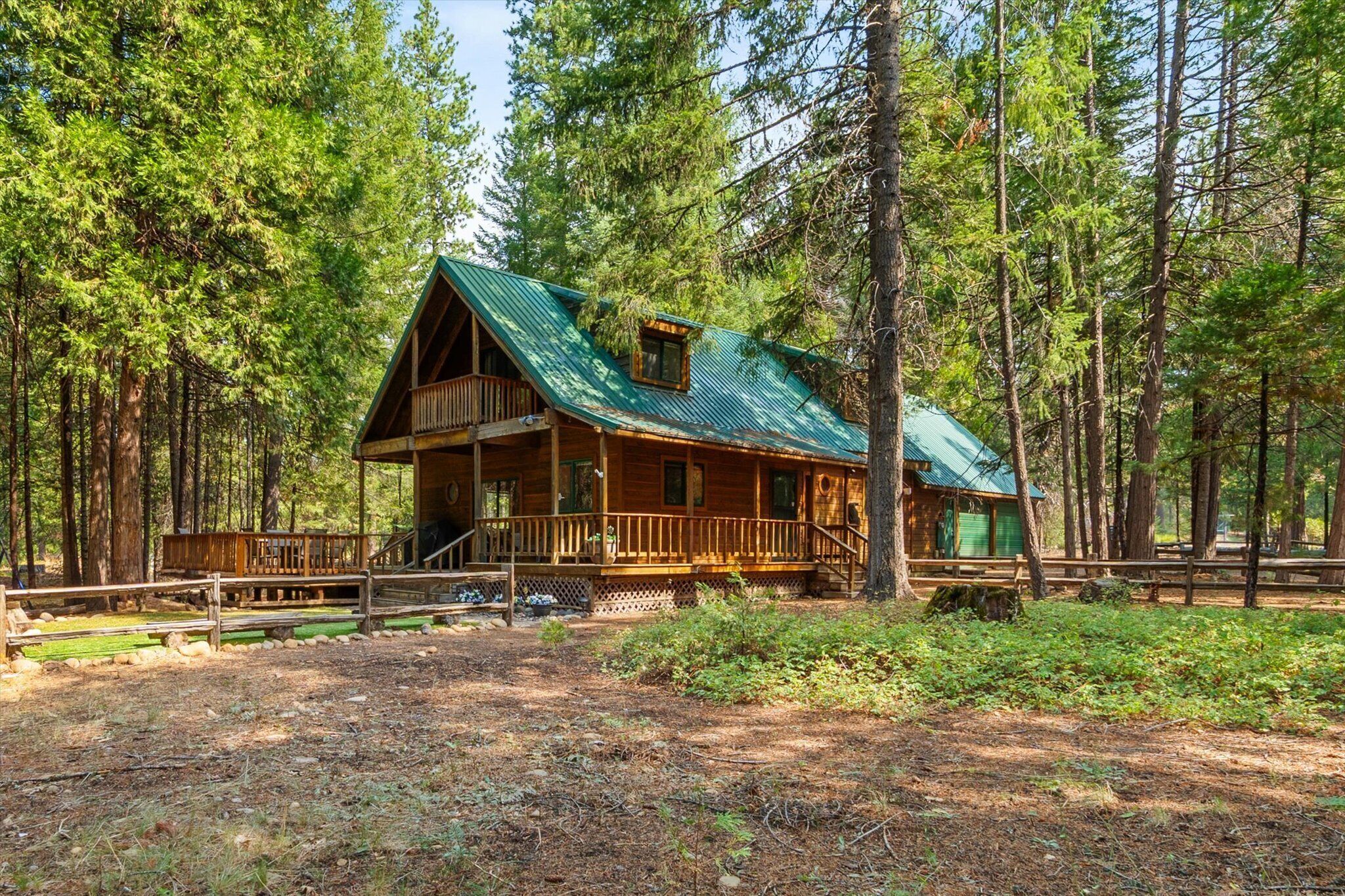 A wooden cabin with a green roof, surrounded by tall pine trees.