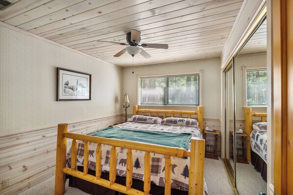 A wooden-framed bed with a quilt, a ceiling fan, a window with blinds, and a framed picture on the wall.