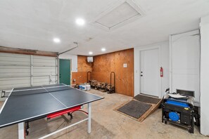 A room with a ping pong table, a door, a fire extinguisher, and a generator.
