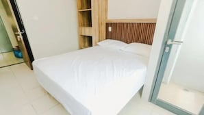 A single-bed room with a wooden headboard, a glass door, and a tiled floor. - Omega Rooms Riverdale by Buka Kamar (Cikarang/Bekasi)