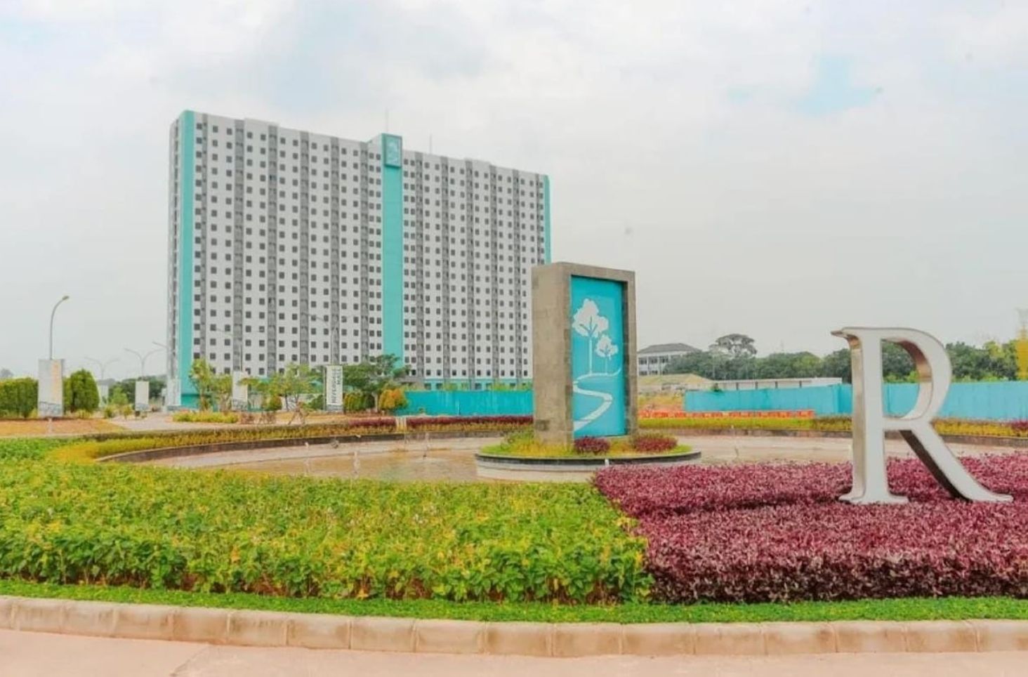 A large residential building with a modern design, surrounded by landscaped gardens and a prominent 'R' sign.