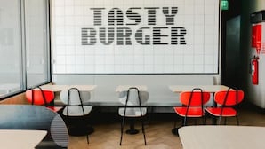 A restaurant interior with a large sign reading 'TASTY BURGER' on the wall, tables with chairs, and a fire extinguisher on the wall. - Omega Rooms Riverdale by Buka Kamar (Cikarang/Bekasi)