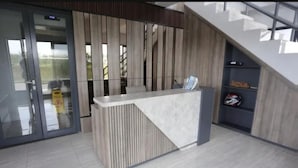 A reception desk with a modern design, a staircase, and a glass door entrance. - Omega Rooms Riverdale by Buka Kamar (Cikarang/Bekasi)