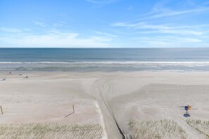 Uma praia com céu claro, ondas suaves e algumas pessoas ao longe.