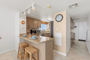 Cozinha moderna com ilha central, banquetas de madeira, um relógio e uma geladeira.