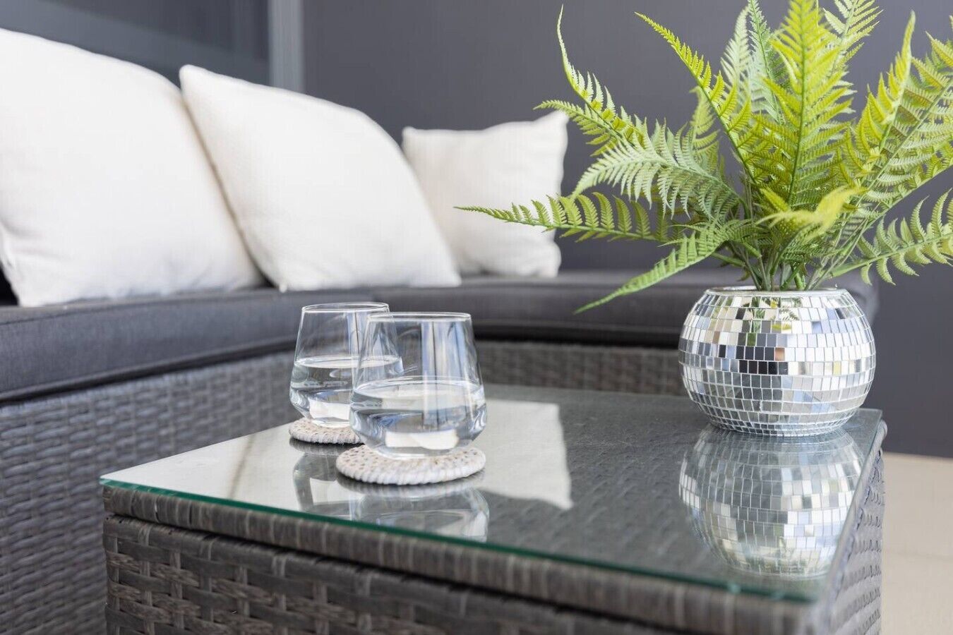 A glass-top table with two clear glasses and a disco ball vase.