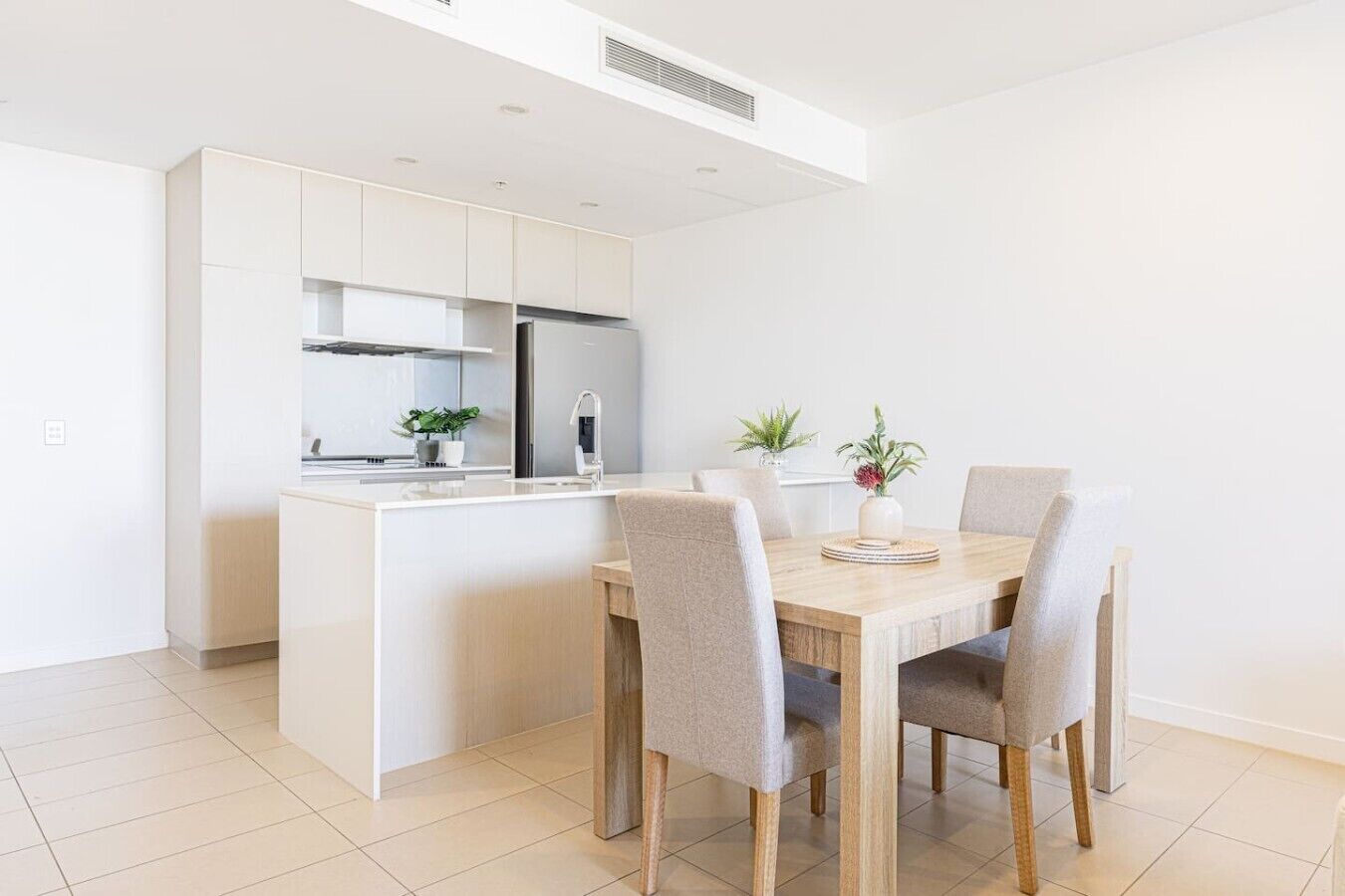 A modern kitchen with white cabinetry, a central island, and a dining area with a wooden table and chairs.