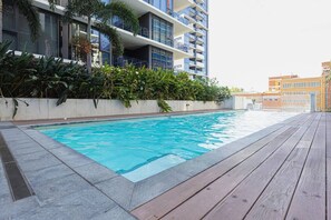 A swimming pool with a wooden deck, surrounded by a building with balconies and greenery. - Stylish Milton Pad - Sweeping River Views & Pool (Milton)