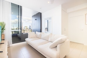 A modern living room with a sofa, a view of a cityscape through large windows, and a balcony. - Stylish Milton Pad - Sweeping River Views & Pool (Milton)