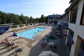 Ein Poolbereich mit Liegestühlen, Sonnenschirmen und einem Gebäude mit Balkon mit Blick auf den Pool.