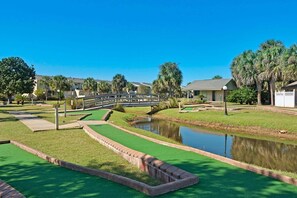 A golf course with a bridge, a pond, and residential buildings in the background. - Gulf Highlands Studio Getaway | King Bed, Bunks, Steps to the Beach (Panama City Beach)