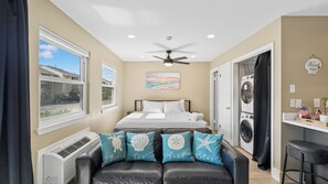 A bedroom with a bed, a ceiling fan, a painting, a laundry area, and a view of the outside. - Gulf Highlands Studio Getaway | King Bed, Bunks, Steps to the Beach (Panama City Beach)