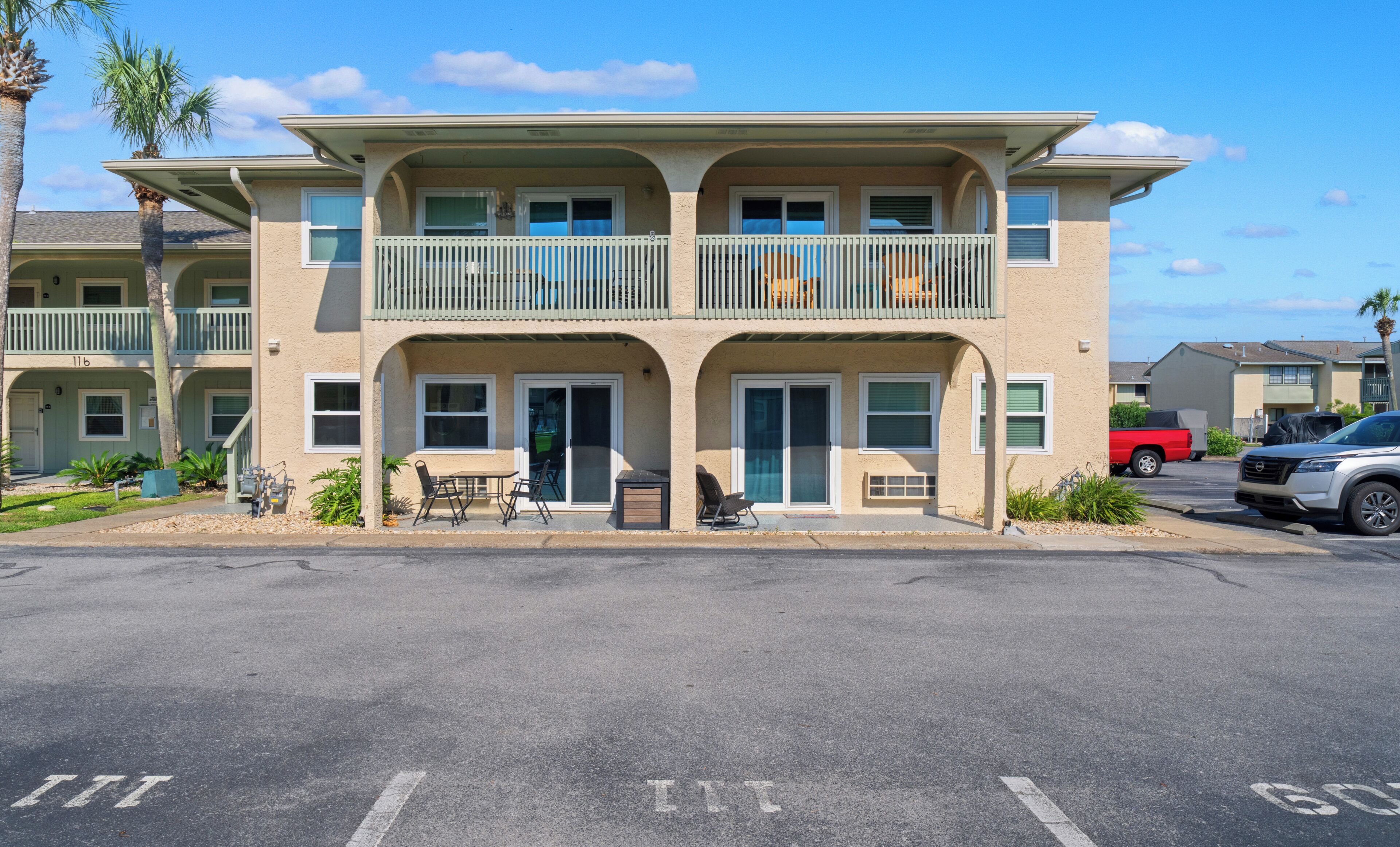 A multi-story hotel with a balcony on the second floor, outdoor seating, and a parking lot in front.