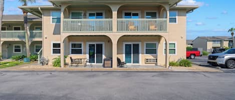A multi-story hotel with a balcony on the second floor, outdoor seating, and a parking lot in front.