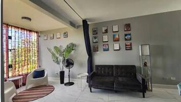 Un salon comprenant un canapé, des fauteuils, un ventilateur, une plante en pot et un mur orné de tableaux encadrés.