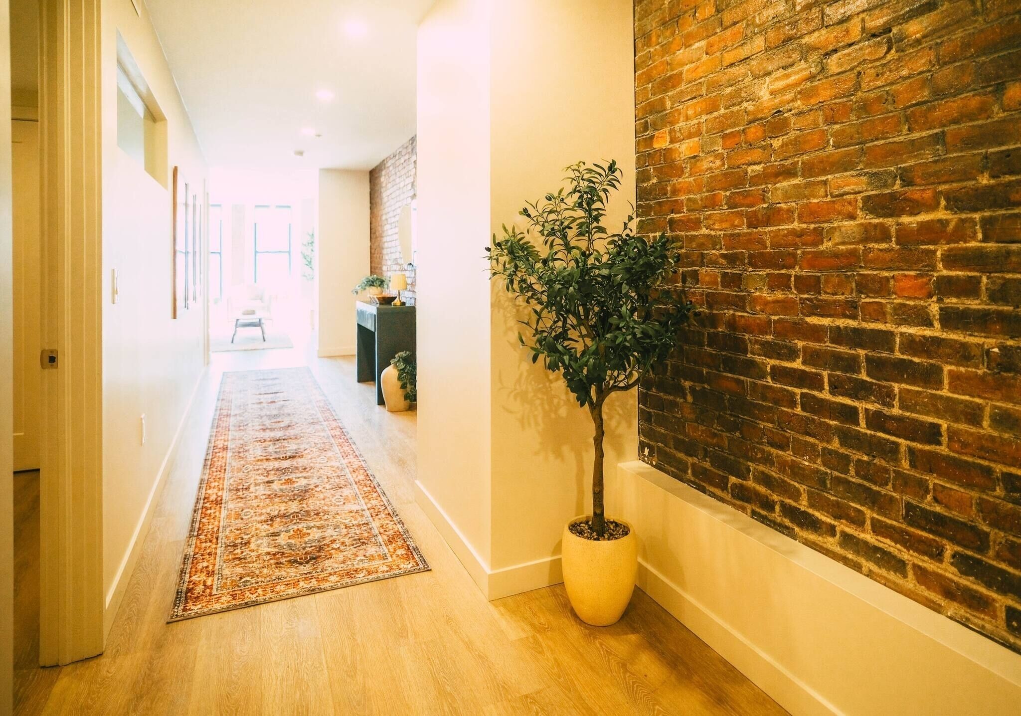 A hallway with a wooden floor, a brick wall, and a potted plant.