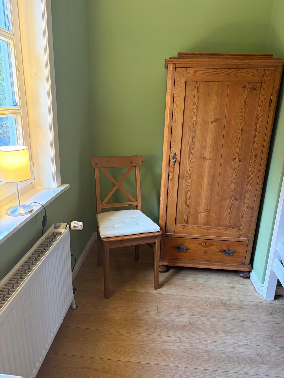 A room with a radiator, a wooden chair, and a wooden cabinet.