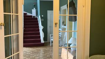 A hallway with a wooden herringbone floor, a white door with glass panels, and a staircase leading to an upper level.