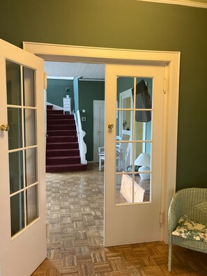 A hallway with a wooden herringbone floor, a white door with glass panels, and a staircase leading to an upper level.