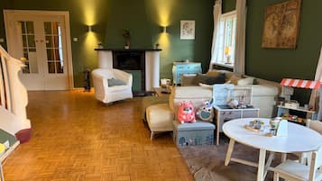 Un salon chaleureux avec une cheminée, un canapé, une table à manger avec des chaises et un petit coin jeux avec des jouets.
