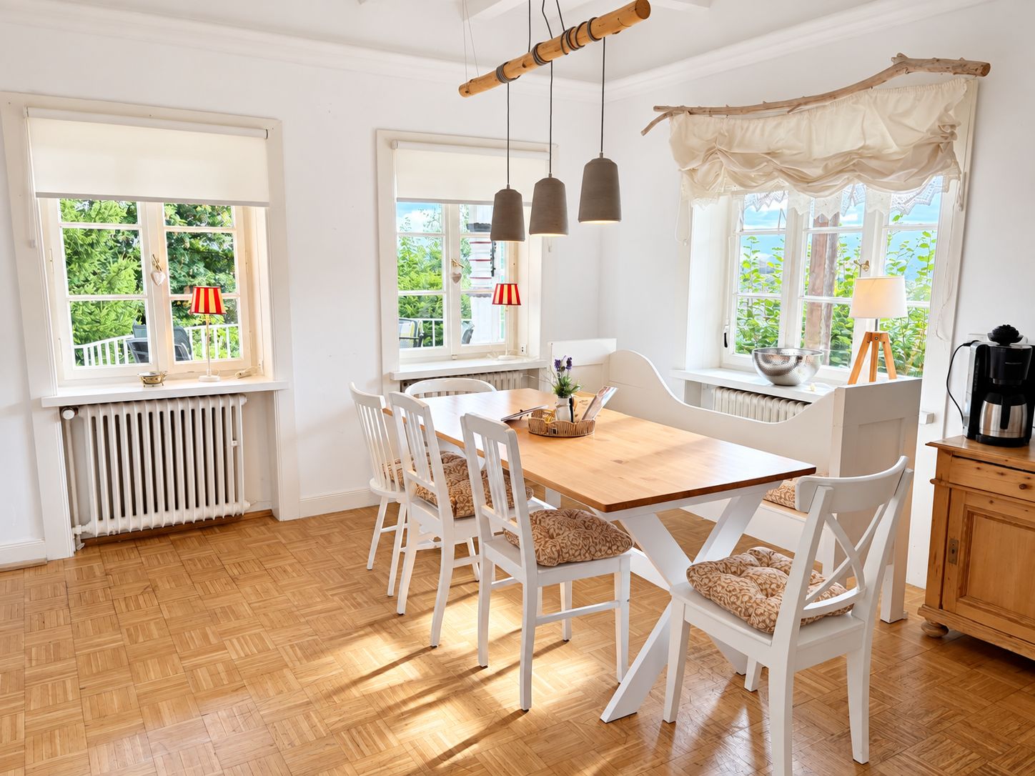 Un comedor con una mesa de madera, sillas blancas y luces colgantes.
