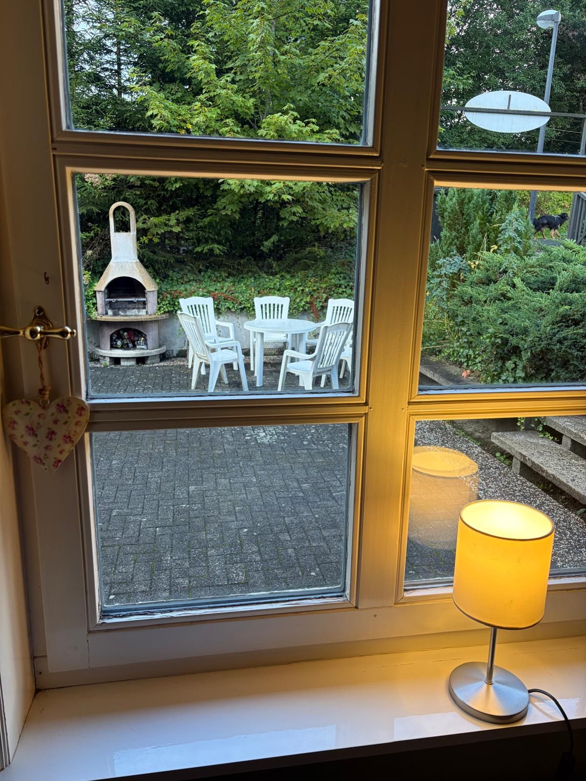 A window with a view of an outdoor seating area with white chairs and a stone fireplace.