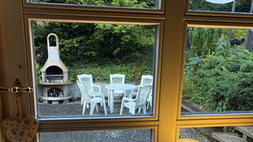 A window with a view of an outdoor seating area with white chairs and a stone fireplace.