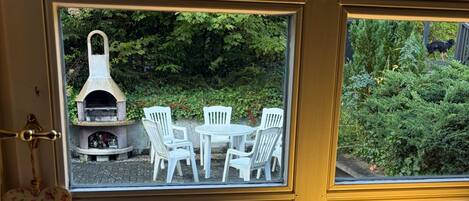 Une fenêtre donnant sur un espace extérieur aménagé avec des chaises blanches et une cheminée en pierre.