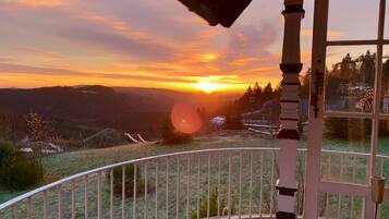 A balcony with a view of a sunset over a hilly landscape.