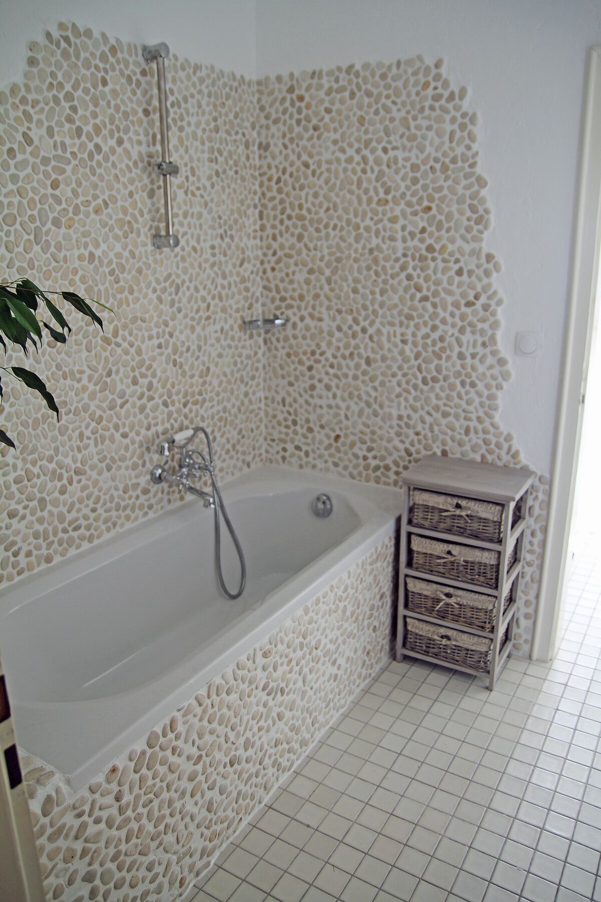 Ein Badezimmer mit rauen Wandfliesen, einer Badewanne und einem kleinen Holztisch.