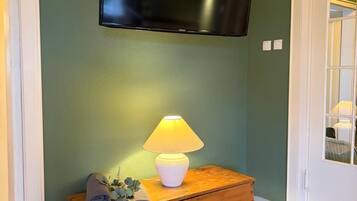 A room with a television mounted on the wall, a wooden chest of drawers, and a lamp on top.