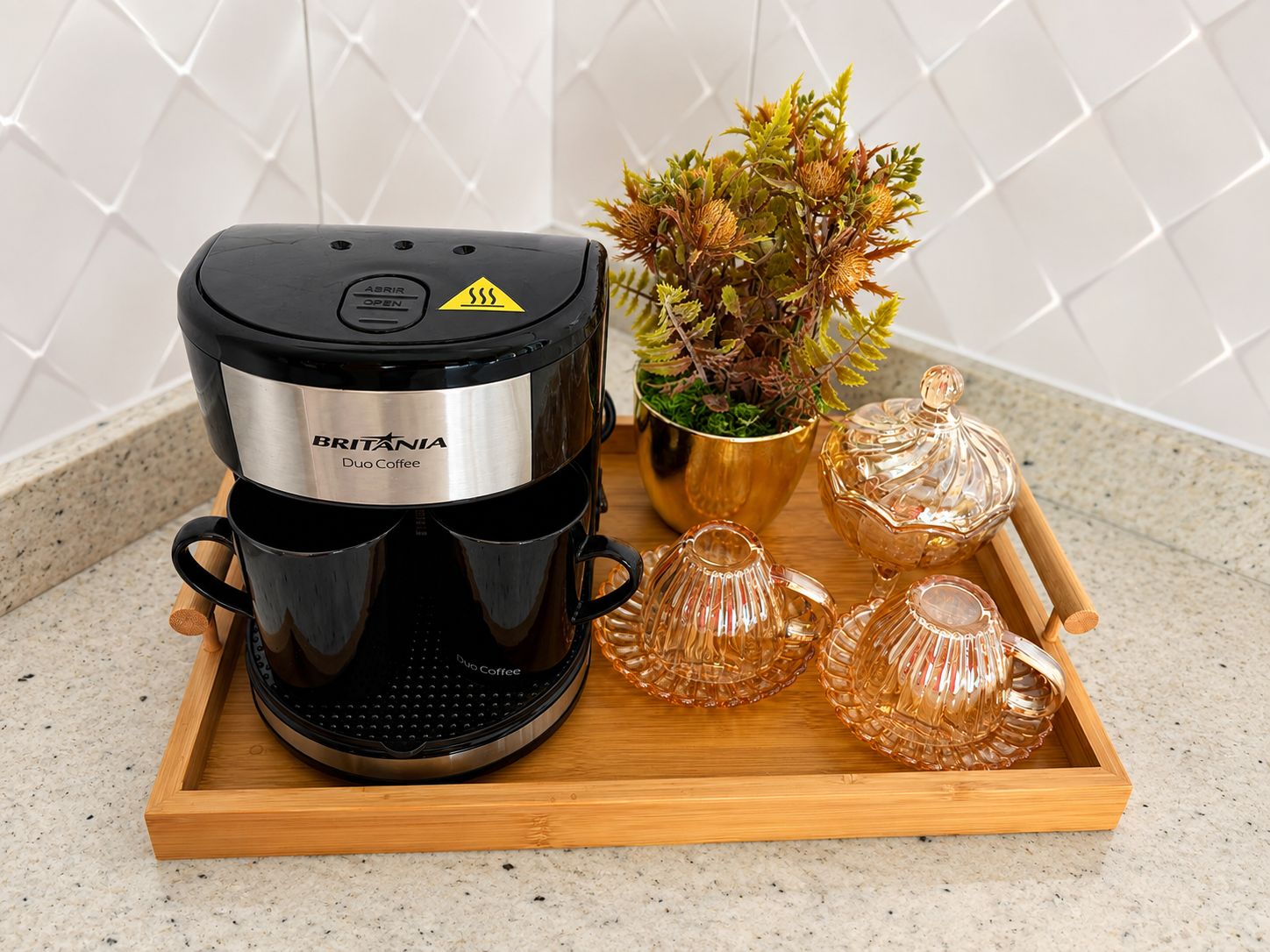 Uma cafeteira em um tabuleiro com copos de vidro e uma planta.