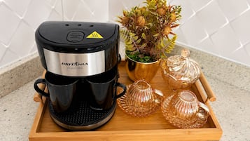 Uma cafeteira em um tabuleiro com copos de vidro e uma planta.
