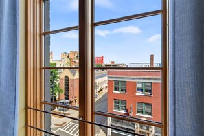 A window with a view of a cityscape, including a red brick building with 'IMPERIAL LIFE INSURANCE' signage. - Historic Downtown Loft | Steps from S&W Food Hall & Drum Circle! (Asheville)